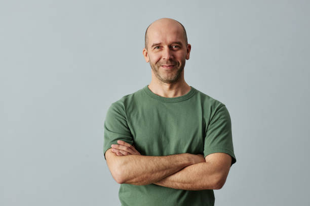 Minimal waist up portrait of mature bald man smiling at camera while standing confidently with arms crossed, copy space